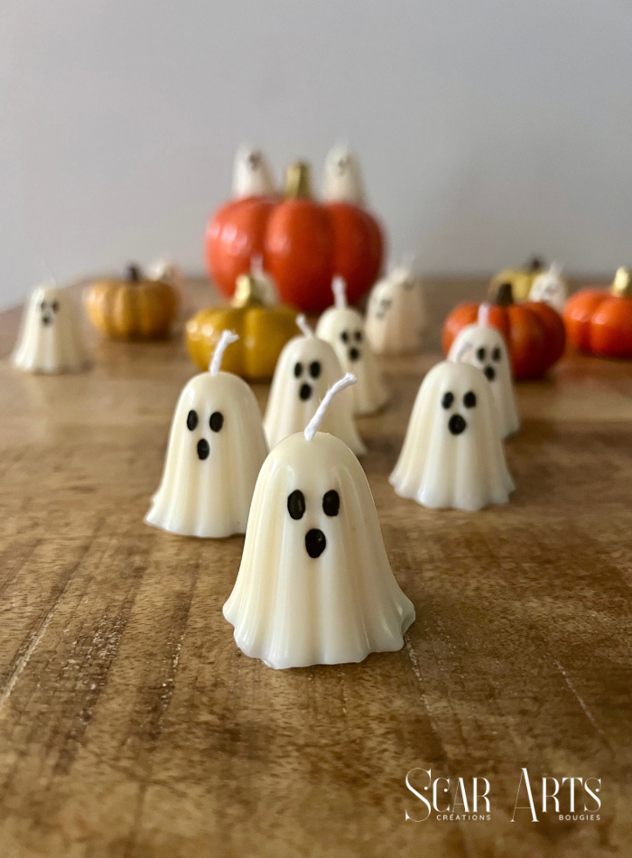 Bougie petit fantôme blanc non allumée, avec une mèche blanche et un visage noir, devant d’autres fantômes et des citrouilles.
