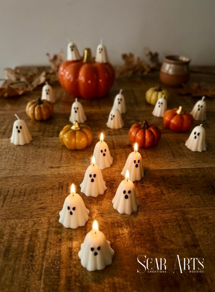 Plusieurs bougies fantômes blanches allumées sur une table en bois, au milieu de citrouilles et de feuilles dans une ambiance tamisée.